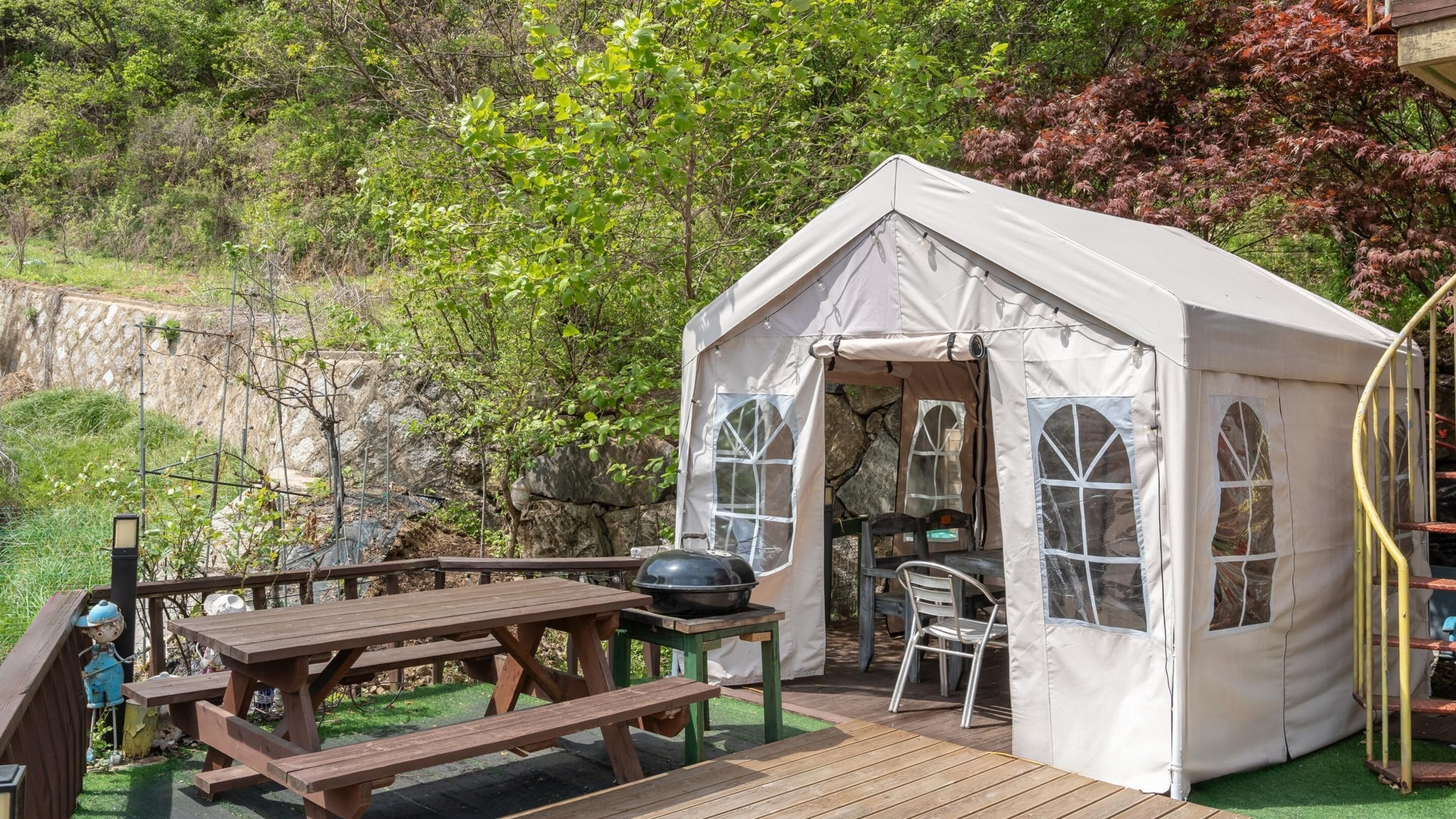 A tent with a small porch, a picnic table, and a grill.