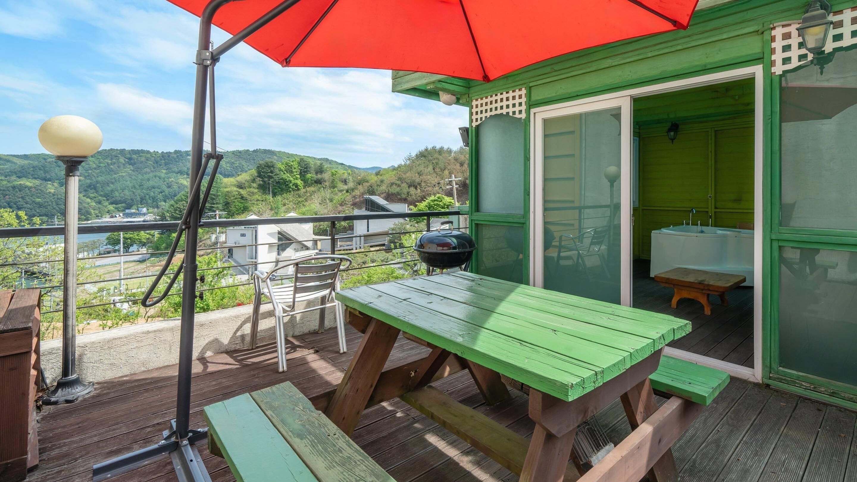 A green wooden deck with a picnic table and chairs, a barbecue grill, and a view of the surrounding landscape.