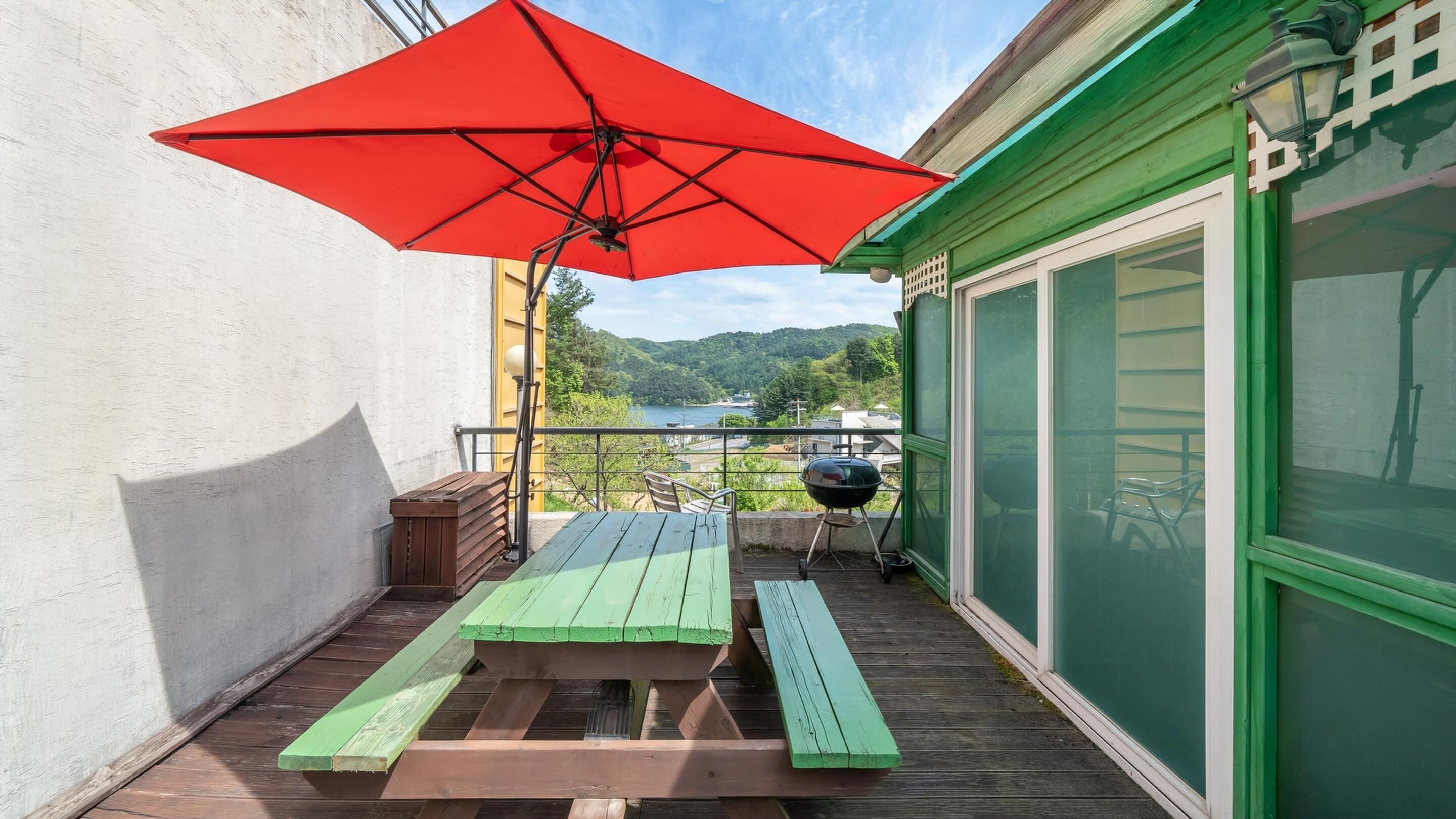 A wooden deck with a picnic table and a red umbrella.