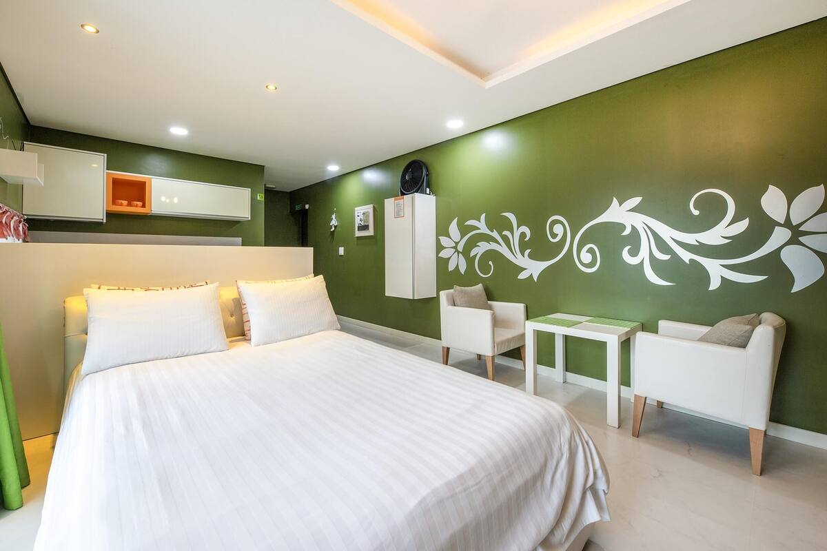 Une chambre moderne avec un grand lit, une petite table, deux chaises et un motif décoratif sur le mur.