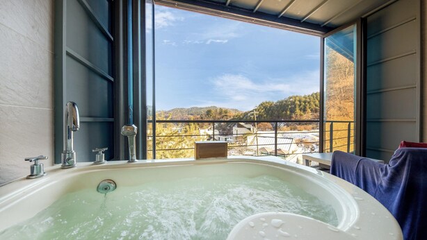 Un baño con una bañera grande, una ventana con vista a un paisaje nevado y un balcón con mesa y sillas.