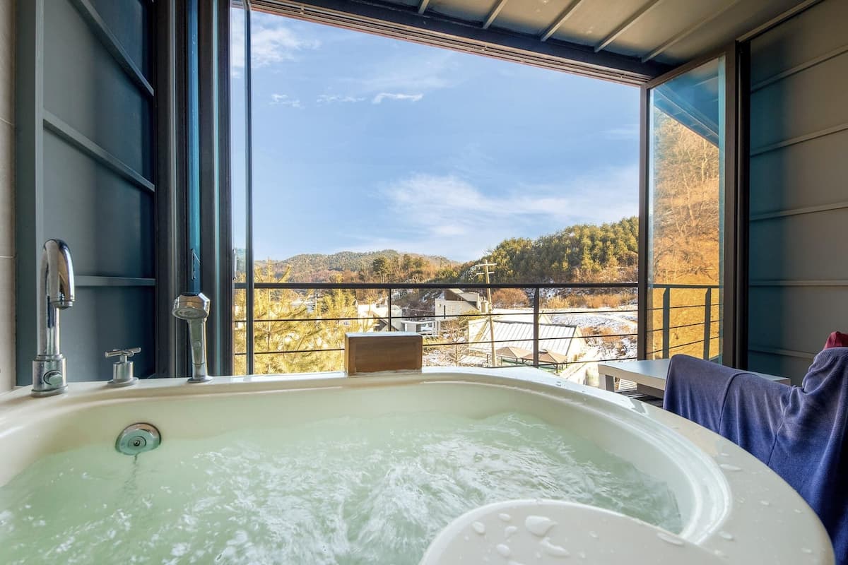 Une salle de bain dotée d’une grande baignoire, d’une fenêtre donnant sur un paysage enneigé et d’un balcon avec une table et des chaises.