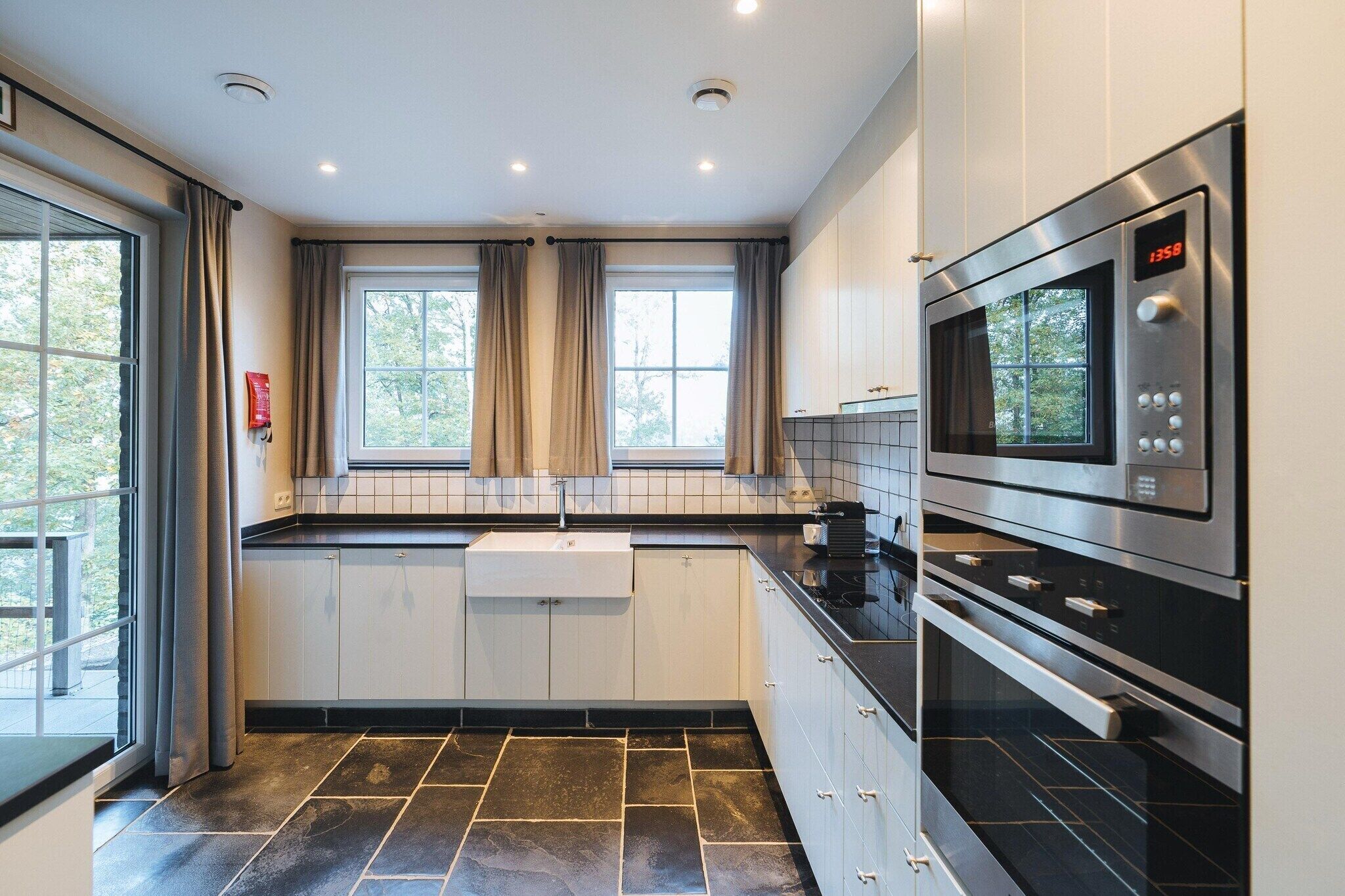 A modern kitchen with a built-in oven, a microwave, and a window with curtains.