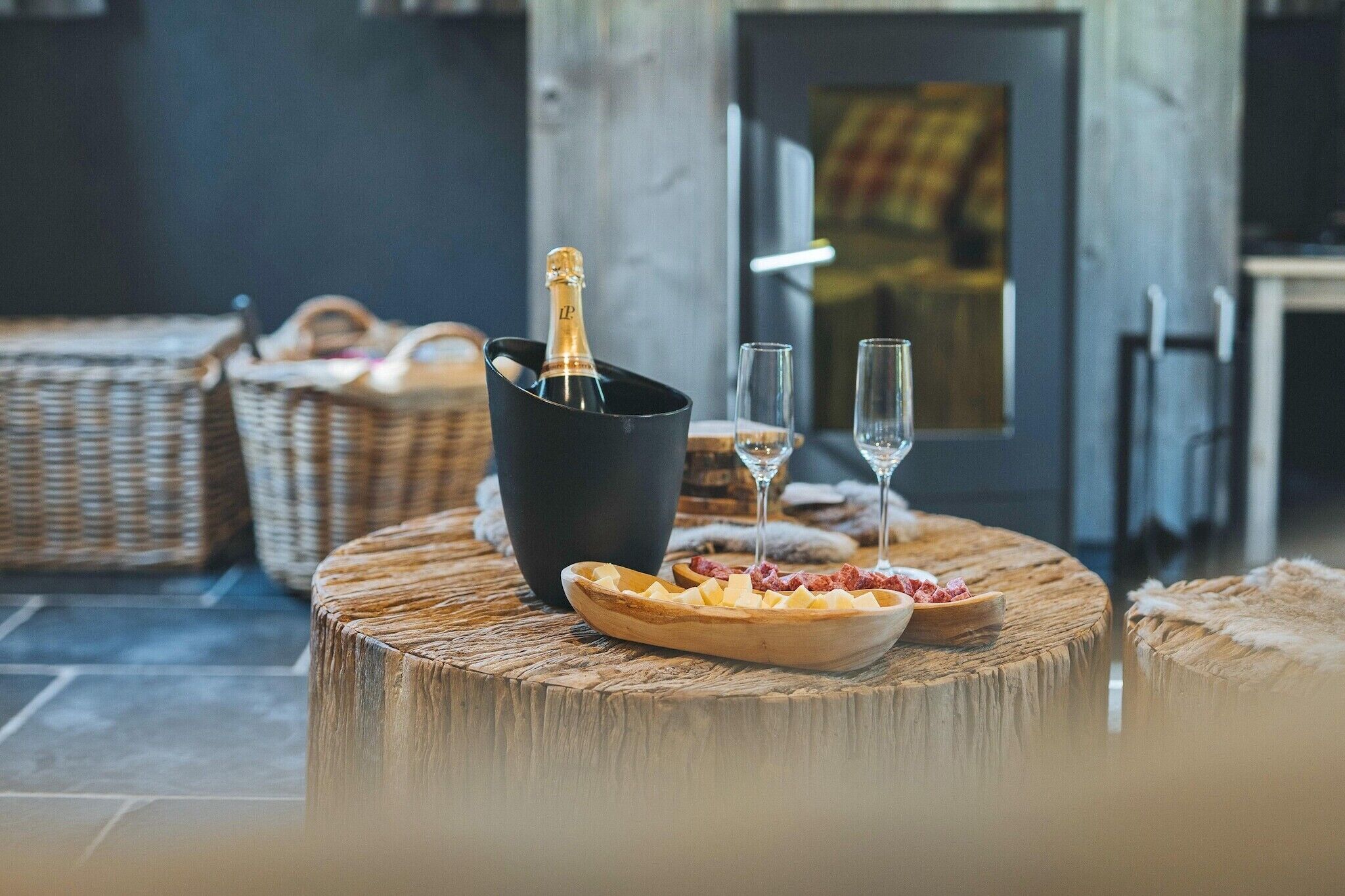 A cozy seating area with wicker furniture, a wooden table with a bowl of snacks, a bottle of champagne, and two glasses.