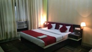 Una habitación de hotel con una cama, una mesita de noche con lámpara y un equipo de aire acondicionado.