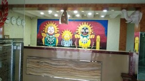 Un área de recepción con un mural de tres soles caricaturescos, relojes en la pared y un mostrador de mármol.