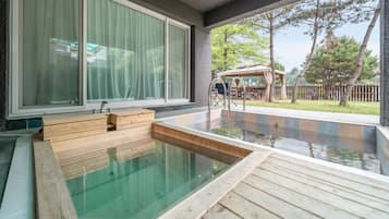 A hot tub with wooden steps, a sliding glass door, and a patio area with outdoor furniture.