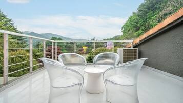 Un balcón con mesa y sillas de vidrio, con vistas a un jardín y colinas distantes.