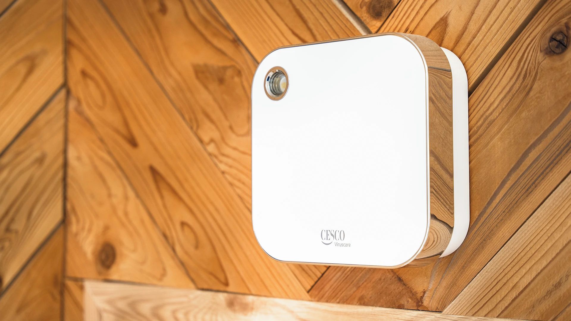 Un dispositivo blanco con cámara y el texto 'CESCO Virtualcare' fijado a una pared de madera.