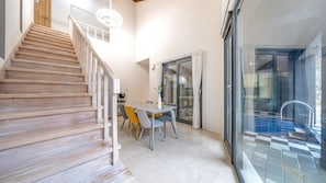 A staircase leading to a dining area with a table and chairs, a glass door leading to an outdoor area, and a modern light fixture.