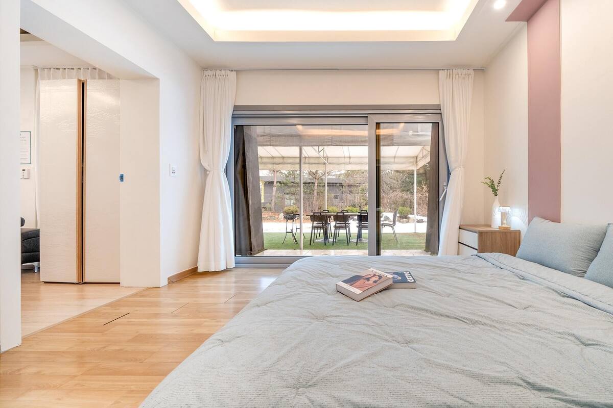 A bedroom with a large bed, a nightstand, and a view of an outdoor patio with a table and chairs.