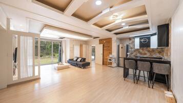 Un amplio salón con cocina moderna, una zona de comedor con taburetes de bar y un gran ventanal corredero que da a un jardín.