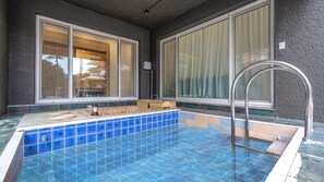 A small outdoor pool with a wooden bench and a metal ladder, surrounded by large windows with curtains.