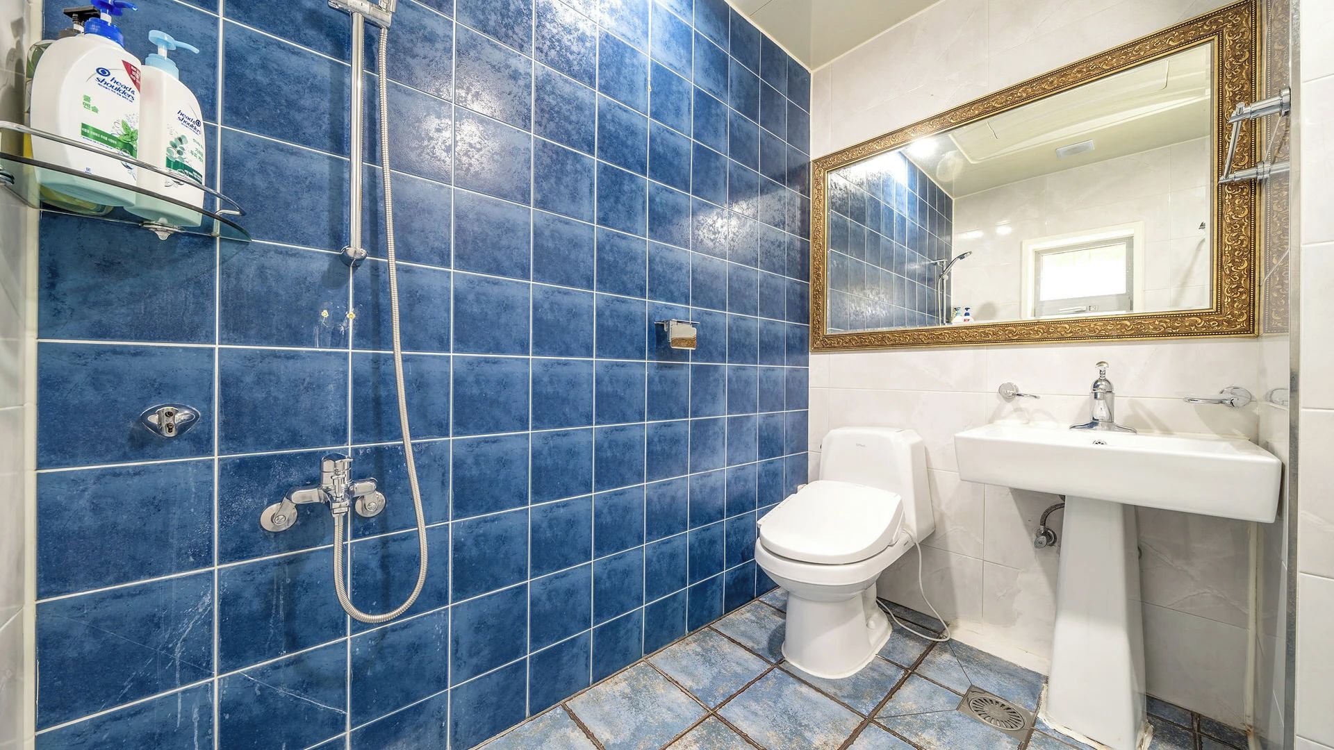 A bathroom with blue tiles, a white toilet, a sink, and a shower with a hose.
