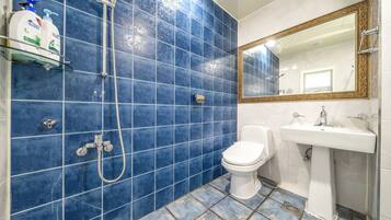 A bathroom with blue tiles, a white toilet, a sink, and a shower with a hose.