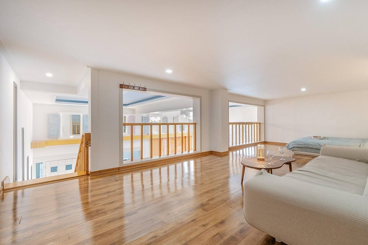 A spacious living room with a large bed, a wooden floor, and a balcony with a railing.