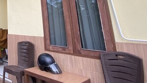 A small wooden table with a helmet on it, two plastic chairs, and a window with curtains.