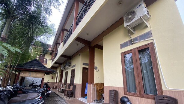 A building with a tiled entrance, a covered area with chairs, and a row of parked motorcycles.