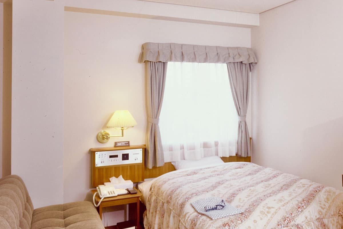 Une chambre d’hôtel avec un lit, une table de chevet avec une lampe, un téléphone et un tiroir de table de chevet.