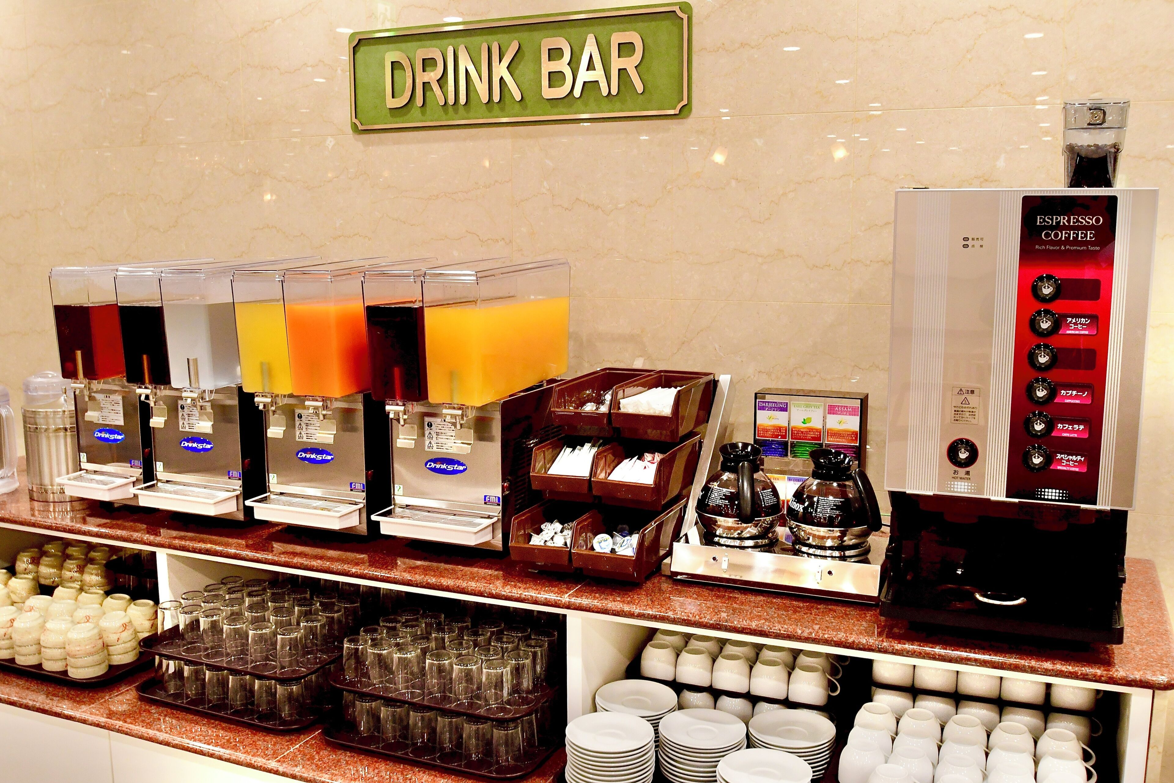 A drink bar with multiple beverage dispensers, coffee machines, and a variety of glassware and cups.