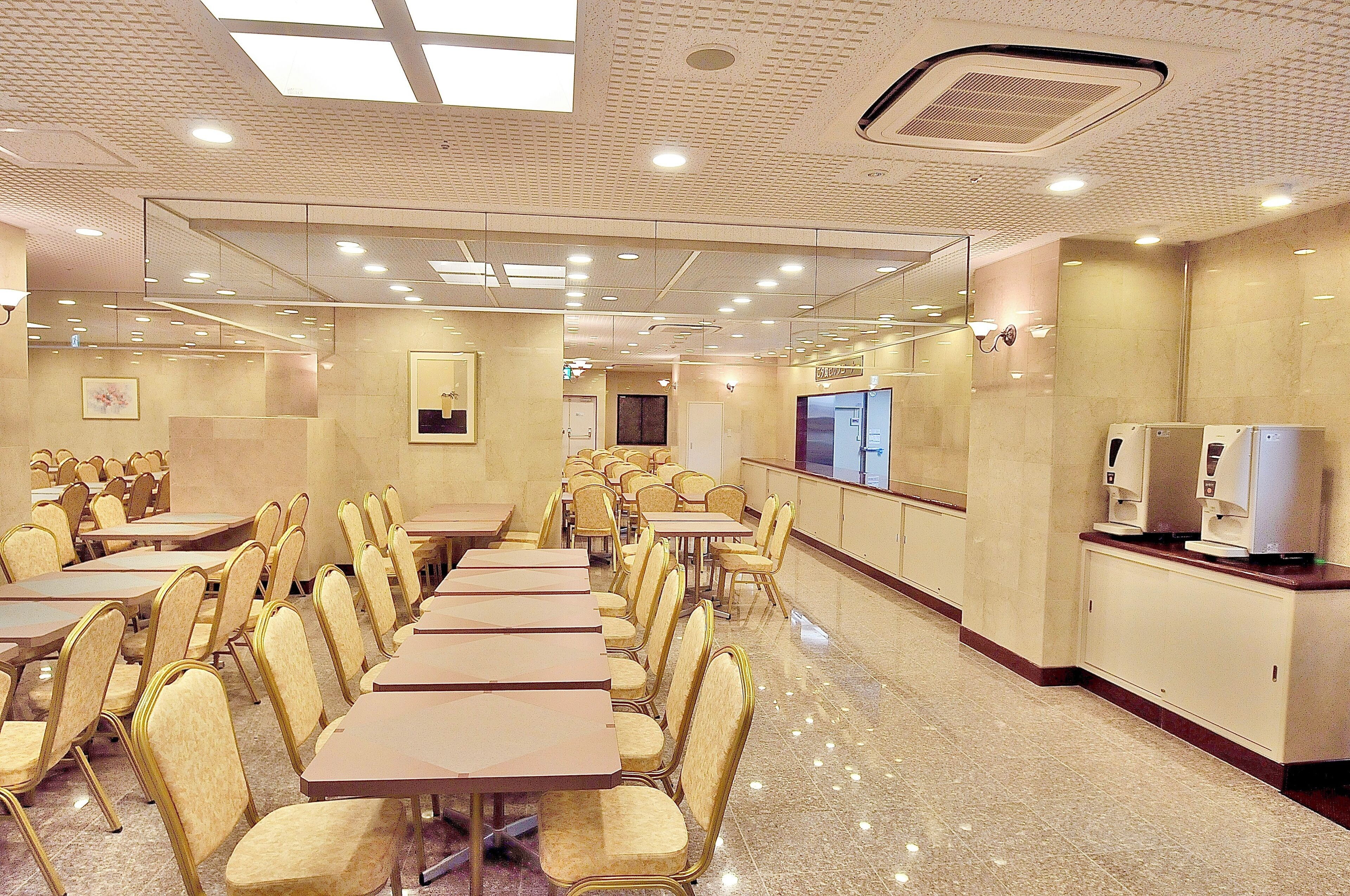 Un salón de conferencias con varias mesas y sillas, una mesa de recepción y un espejo grande en la pared.