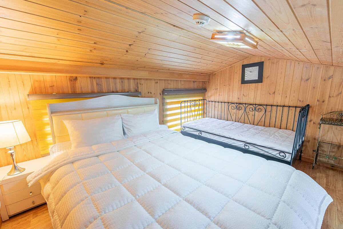 A wooden-paneled room with a bed, a nightstand, and a wall-mounted shelf.