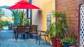 Patio esterno con tavolo e sedie, un ombrellone rosso e piante in vaso.