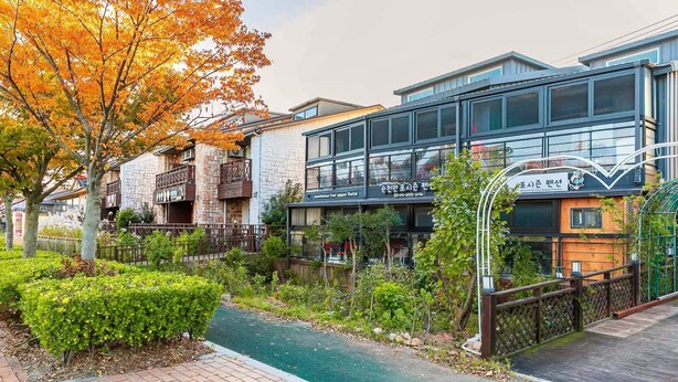 A modern building with a stone facade, a glass entrance, and a sign indicating a pension. - Suncheonman 4Season Pension (Suncheon)