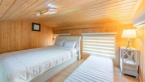 A cozy wooden cabin bedroom with a bed, a bench, a bedside table, and a window with blinds. - Suncheonman 4Season Pension (Suncheon)