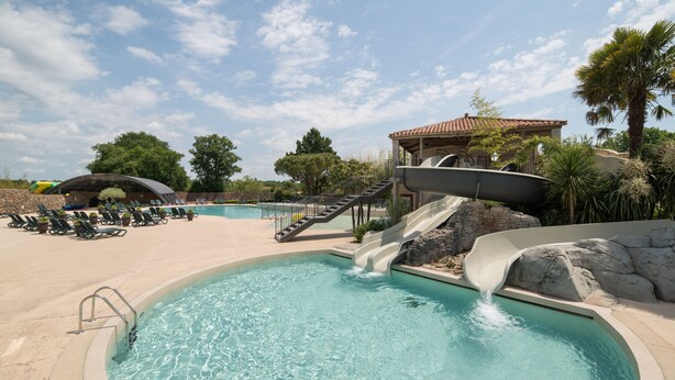A swimming pool with a water slide, lounge chairs, and a covered area with stairs.