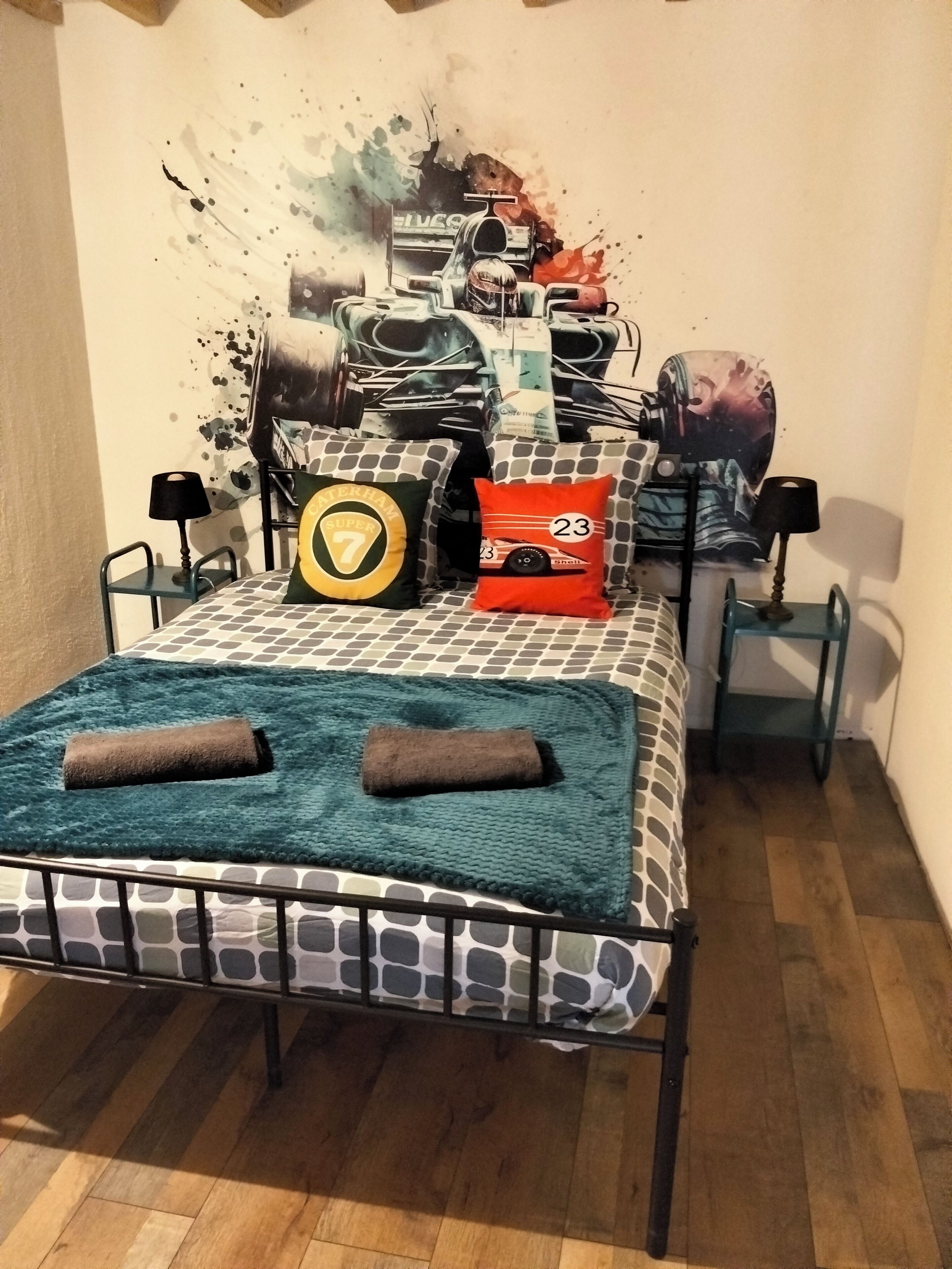 En säng med ett mönstrat överkast, två kuddar, en filt och en väggmålning som föreställer en tävlingsbil.
