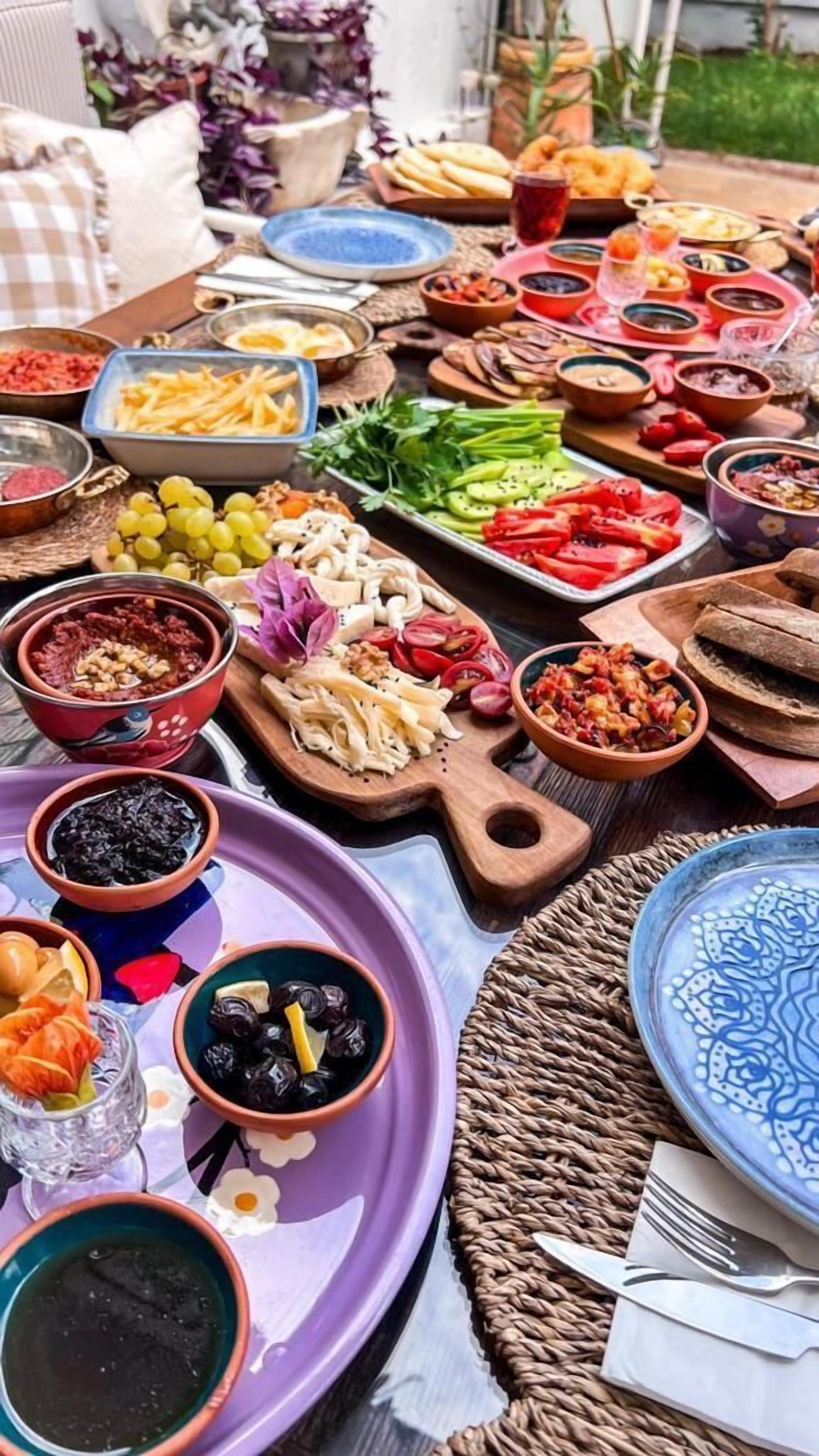A table with various dishes and food items, including fruits, vegetables, and meats, suggesting a communal meal setting.