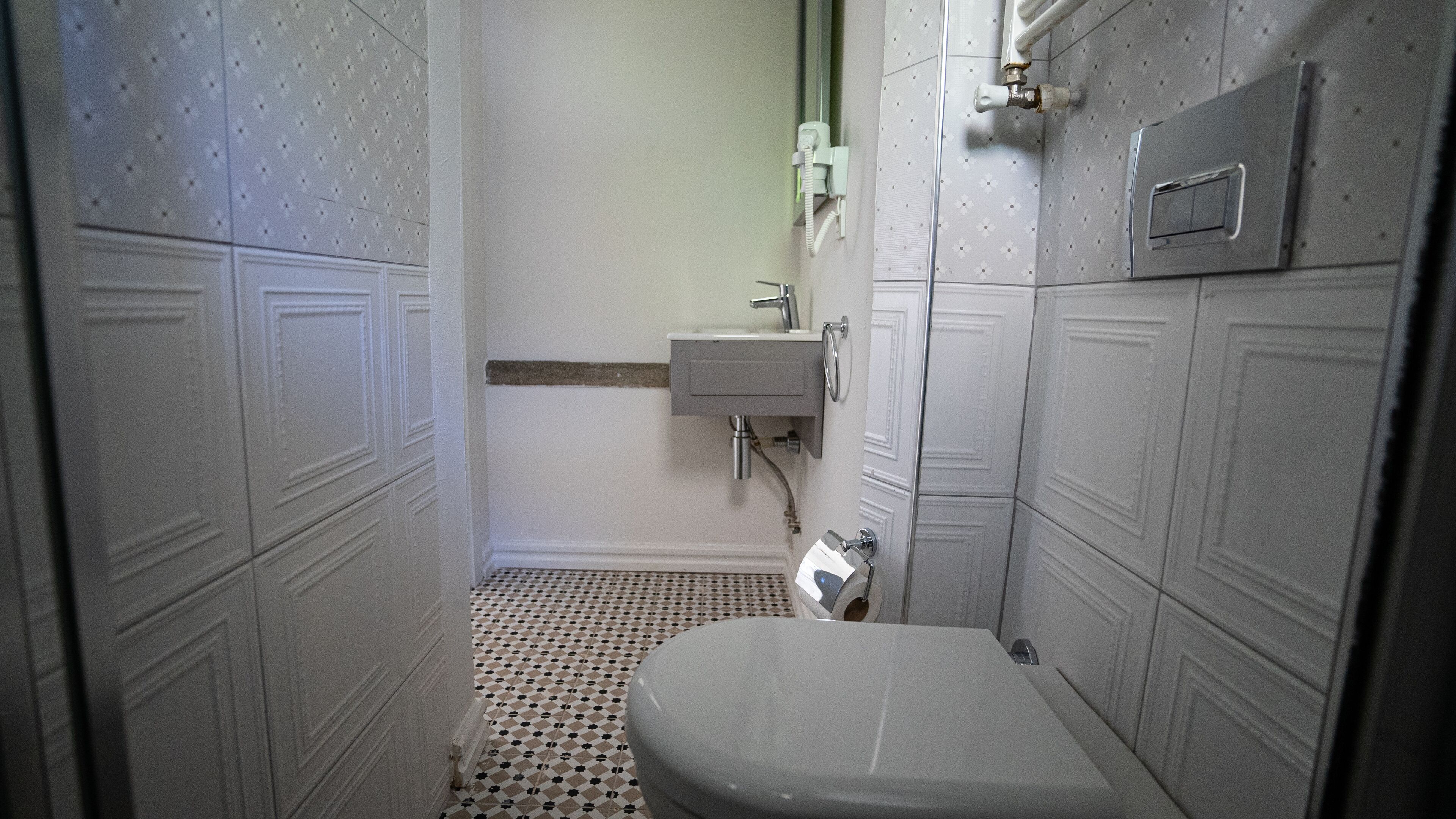A small, narrow bathroom with a toilet, a sink, and a shower.