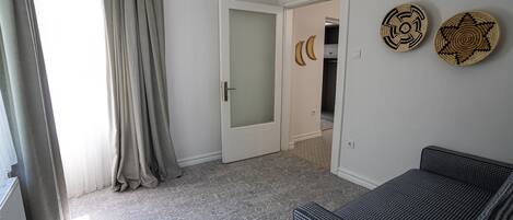 A room with a grey patterned floor, a white door with frosted glass, a grey sofa, and two woven wall decorations.