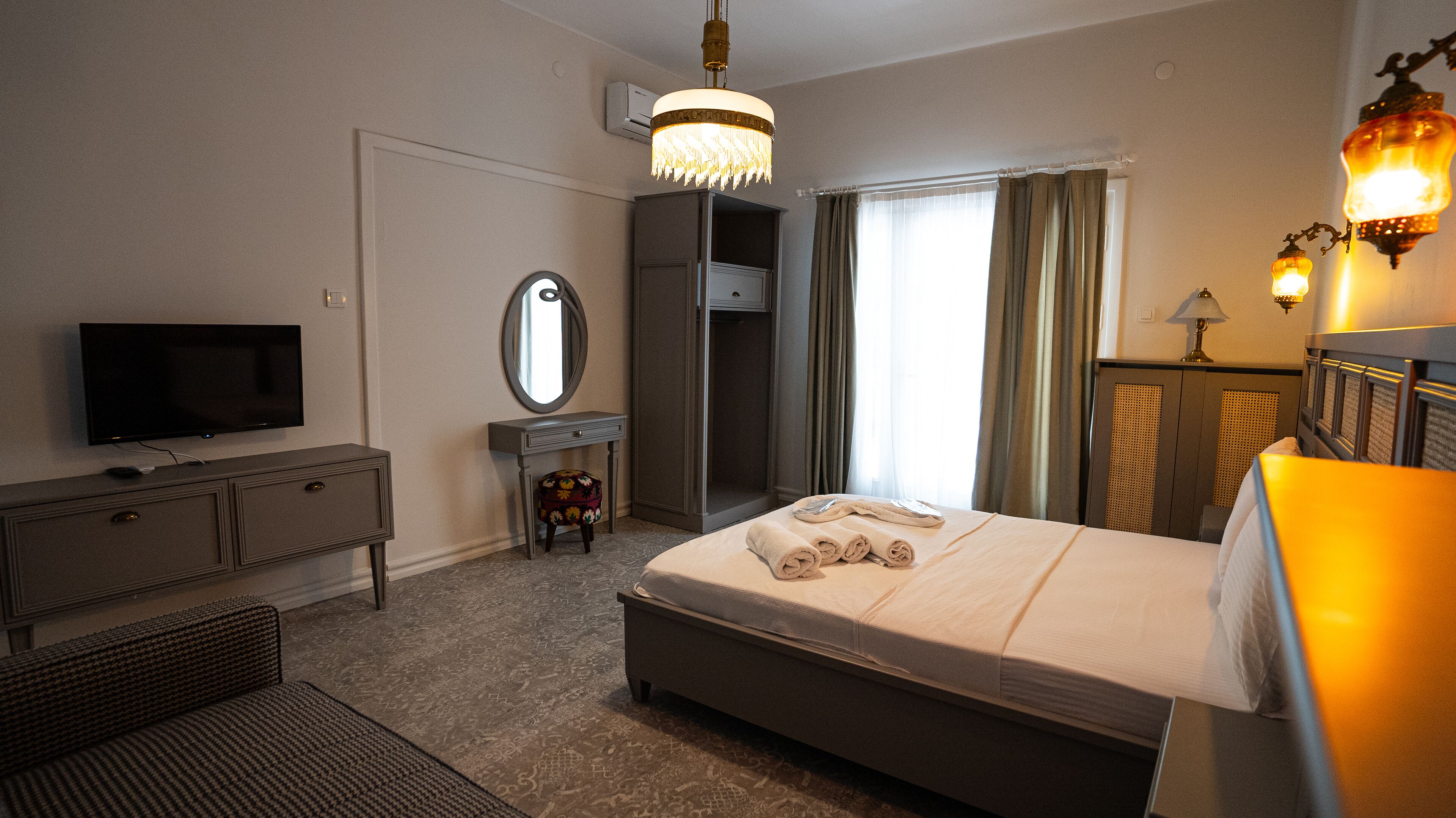 Une chambre d’hôtel avec un lit, une télévision, une commode, un miroir et un lustre.