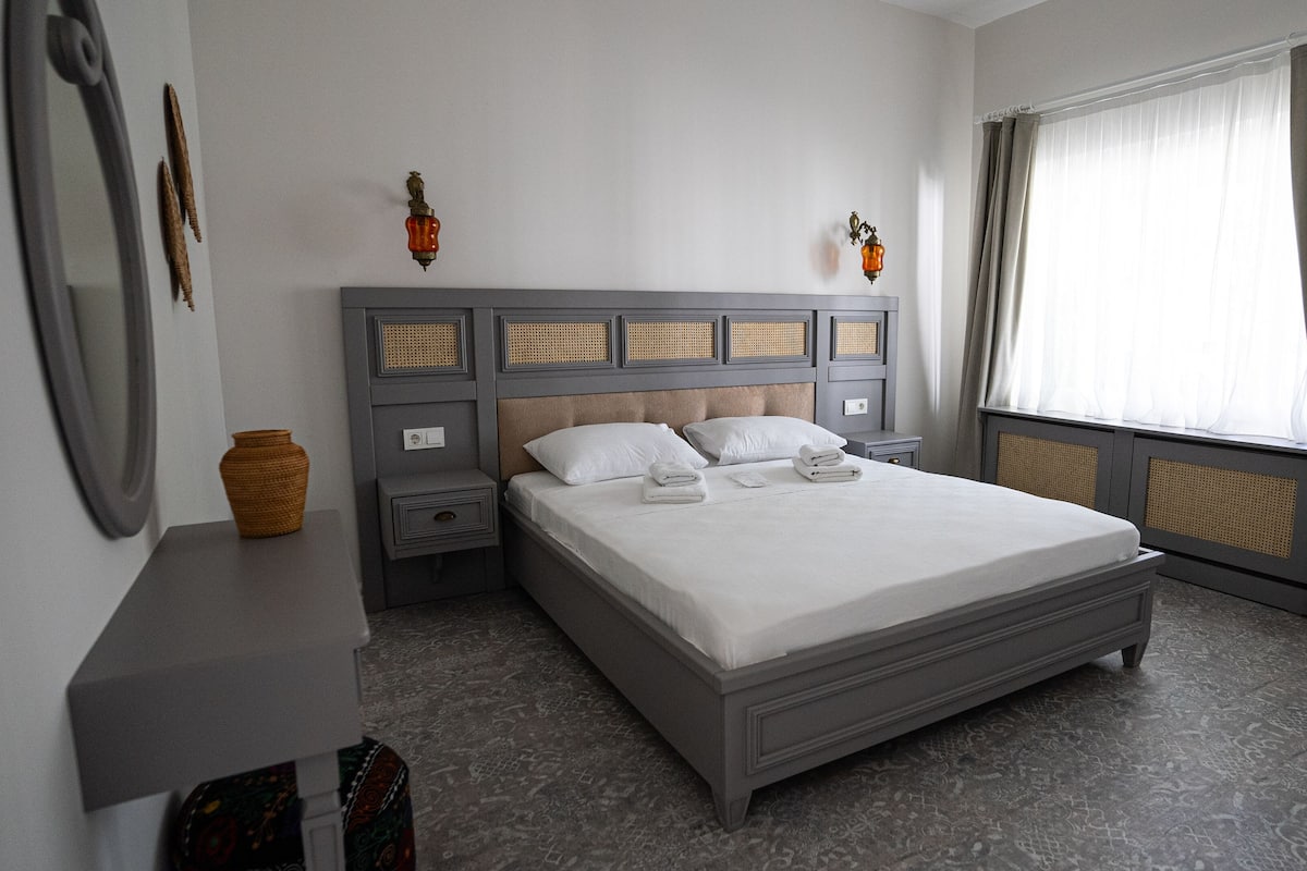 Quarto bem arrumado com uma cama grande, mesa de cabeceira e cortinas na janela.