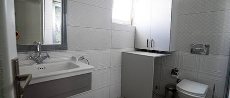 A bathroom with a sink, mirror, cabinet, toilet, and a window.