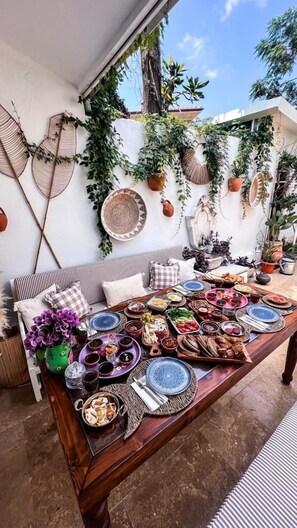 A dining area with a long wooden table set for a meal, surrounded by various plants and decorative items on the walls. - Ece Suit Büyükada (Adalar)