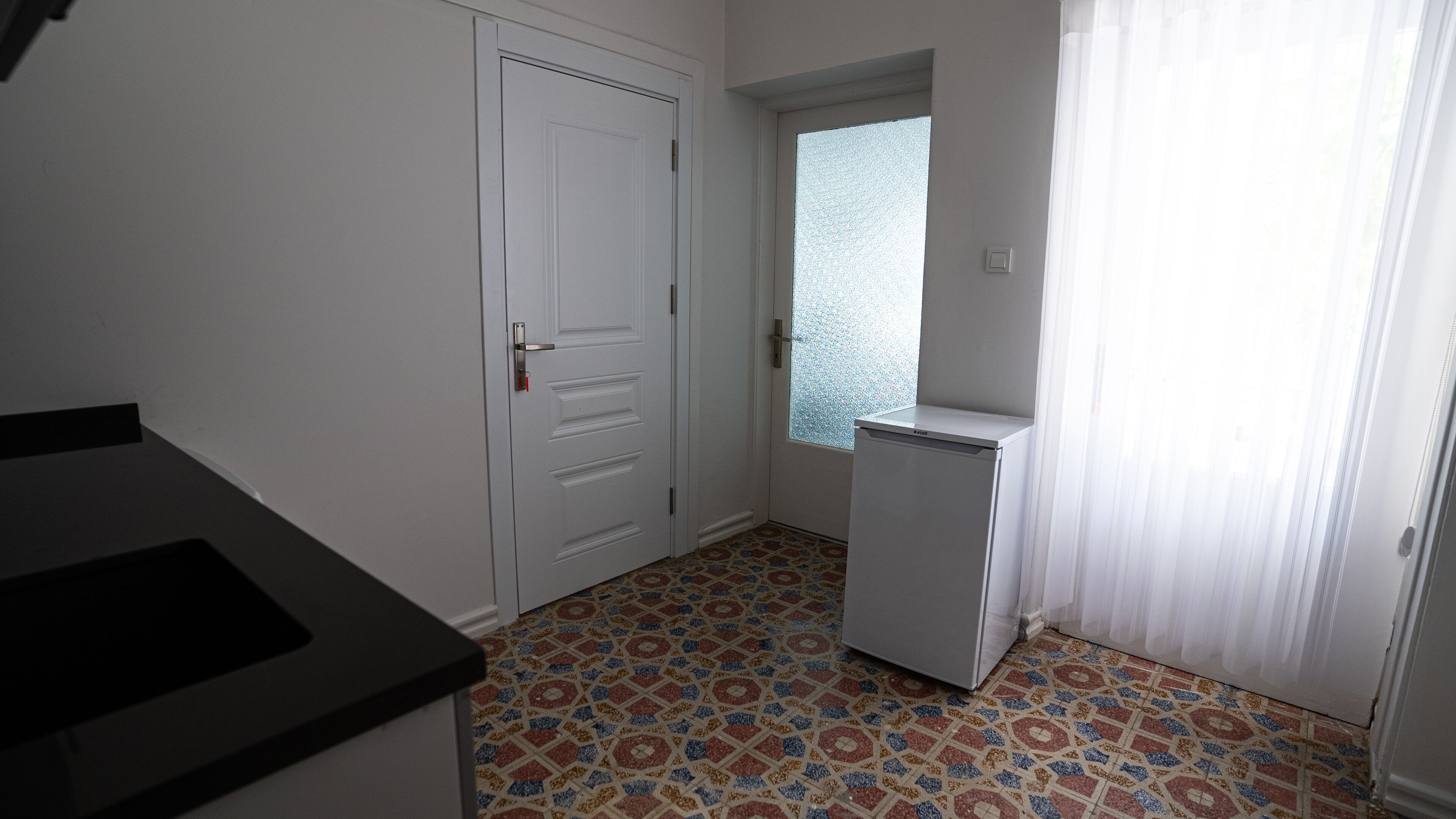 A small, compact kitchen with a refrigerator, a door, and a window with a view.