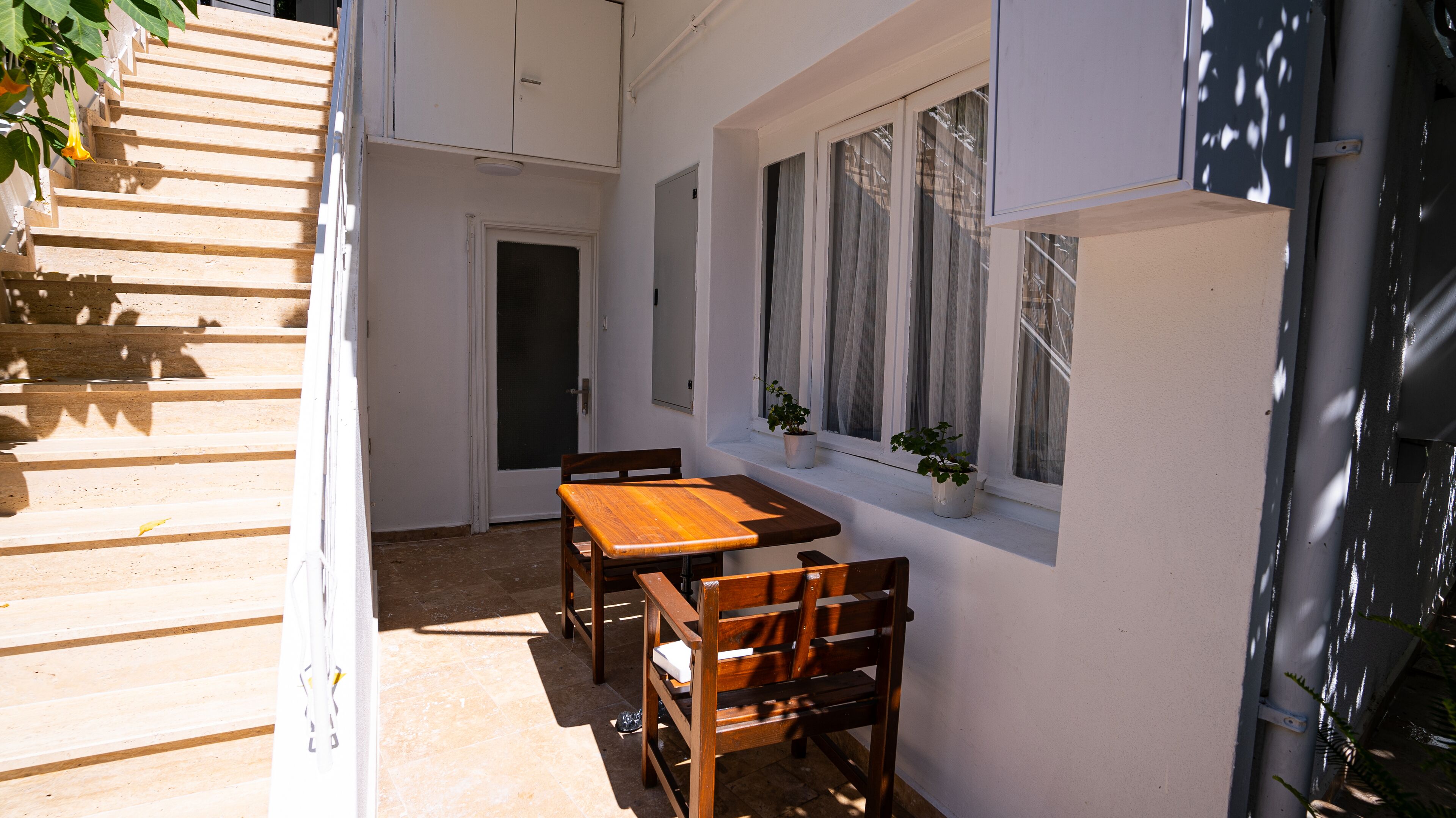 A patio with a wooden table and chairs, a potted plant, and a window with curtains.