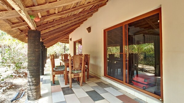 Un patio techado con mesa y sillas de madera, un amplio ventanal corredero y piso de baldosas.