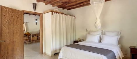 Un dormitorio con cama, dosel, puerta de madera con detalles tallados y un comedor con sillas y mesa.