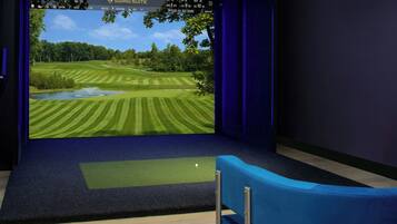 A room with a large screen displaying a golf course view, a blue chair, and a carpeted floor.