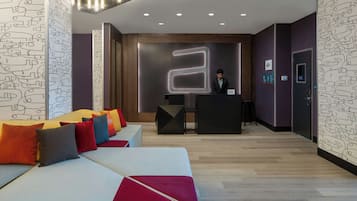 Un moderno vestíbulo de hotel con mostrador de recepción, zona de estar y un gran letrero iluminado.