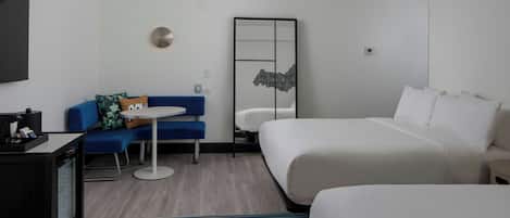 A hotel room with a bed, a desk with a computer, a small table, a sofa, and a colorful striped rug.