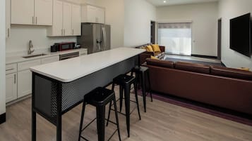 Una cocina moderna con armarios blancos, una isla central con taburetes, un refrigerador y un microondas.