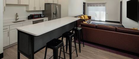 A modern kitchen with white cabinets, a central island with stools, a refrigerator, and a microwave.