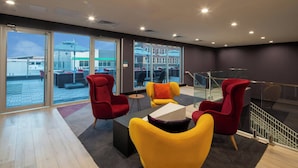 A modern lounge area with a glass wall offering a view of the outside. There are several red and yellow chairs arranged around a central table. - Aloft by Marriott Memphis Downtown (Memphis)