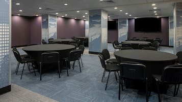 A conference room with multiple tables and chairs, a large screen, and a patterned wall.