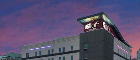 A multi-story hotel with a modern design, featuring a prominent logo at the top.
